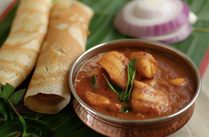 Fish sambal Indian style served with dosa on a banana leaf with onion garnish.