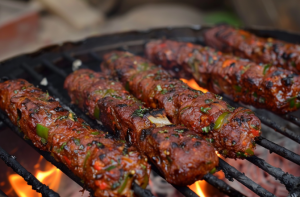 Mutton seekh kebab being cooked on a skewer over a charcoal grill.